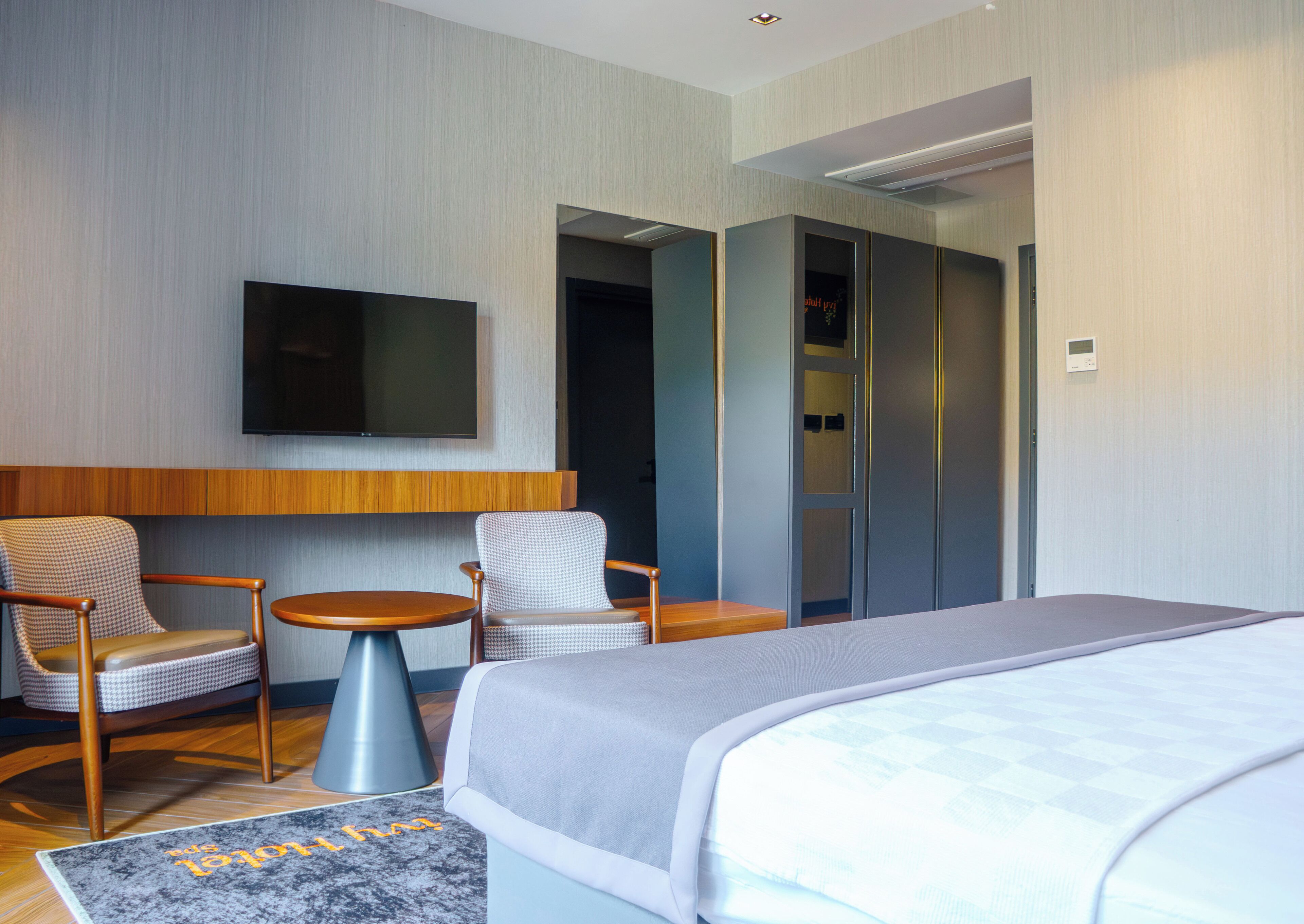 Een moderne hotelkamer met een groot bed, twee fauteuils, een tafeltje, een flatscreen televisie en een kledingkast.
