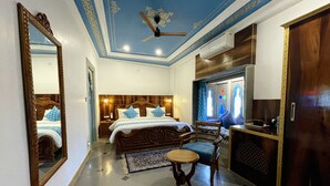 A hotel room with a large bed, a ceiling fan, a wooden wardrobe, and a small table. - Aaj Haveli - A Luxury Boutique Hotel (Udaipur)