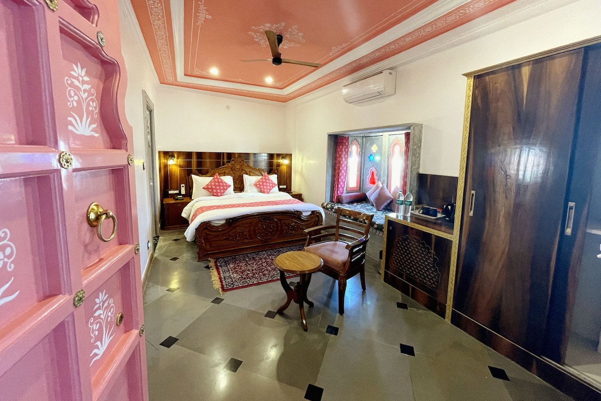 A hotel room with a large bed, a desk, a chair, and a wardrobe.
