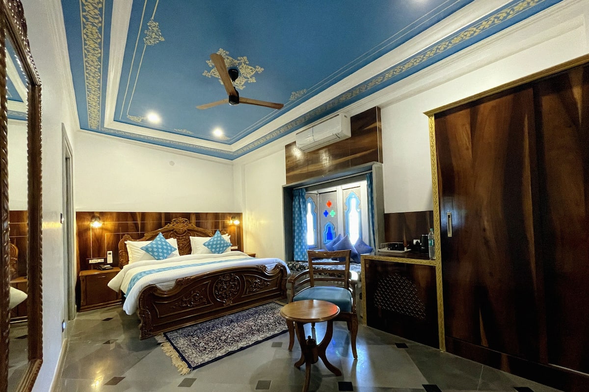 A bedroom with a large bed, a wooden chair, a desk, and a wardrobe.