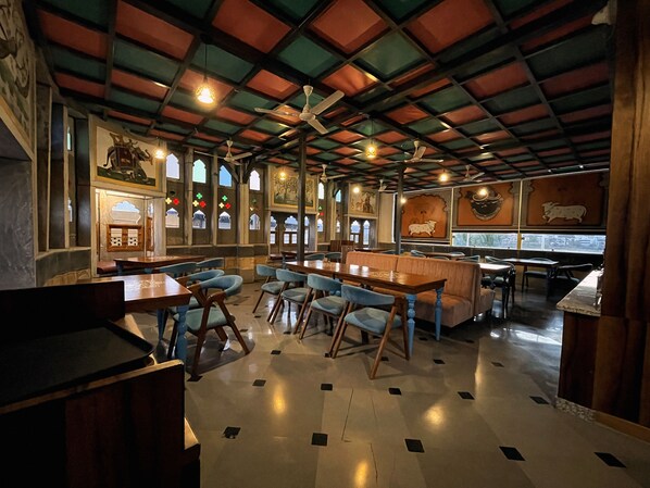 Un restaurant avec un plafond haut, des poutres en bois et différents types de sièges, notamment des tables et des banquettes.