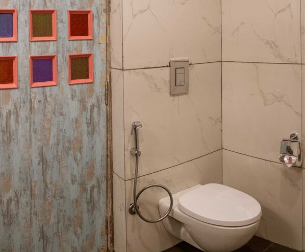 Un baño con inodoro blanco, ducha con cabezal de ducha manual y dispensador de toallas de pared.