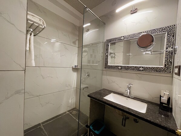 A modern bathroom with a glass-enclosed shower, a marble-tiled wall, a sink with a black countertop, and a decorative mirror. - Aaj Haveli - A Luxury Boutique Hotel (Udaipur)