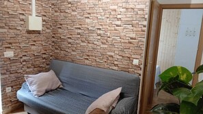 A room with a stone-patterned wall, a grey sofa with cushions, and a potted plant.