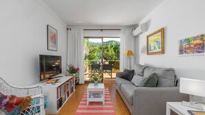 A modern living room with a grey sofa, a white armchair, a TV, and a bookshelf. - Apartment Bougainvillea,  a beautiful apartment just a few steps from the beach. (Port de Sóller)