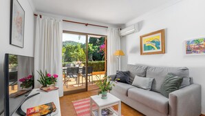 A modern living room with a grey sofa, a flat-screen TV, a small white table with a vase of flowers, and a red rug. - Apartment Bougainvillea,  a beautiful apartment just a few steps from the beach. (Port de Sóller)