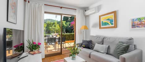 Uma sala de estar moderna com um sofá cinzento, uma TV de tela plana, uma pequena mesa branca com um vaso de flores e um tapete vermelho.