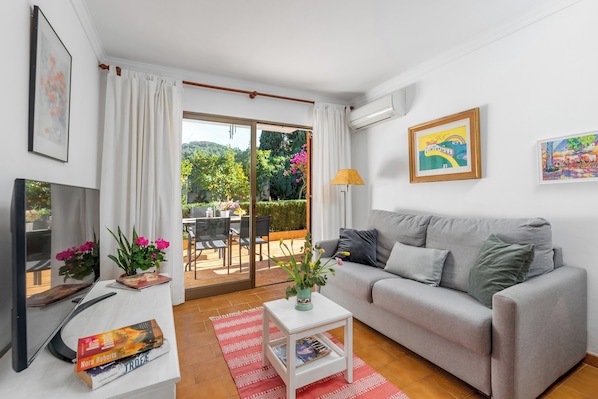 Una sala de estar moderna con un sofá gris, un televisor de pantalla plana, una mesita blanca con un florero y una alfombra roja.