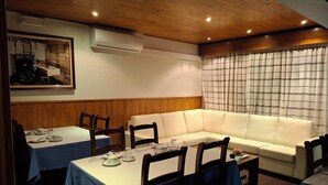 Un comedor con mesas dispuestas para cuatro, un sofá y techo de madera.
