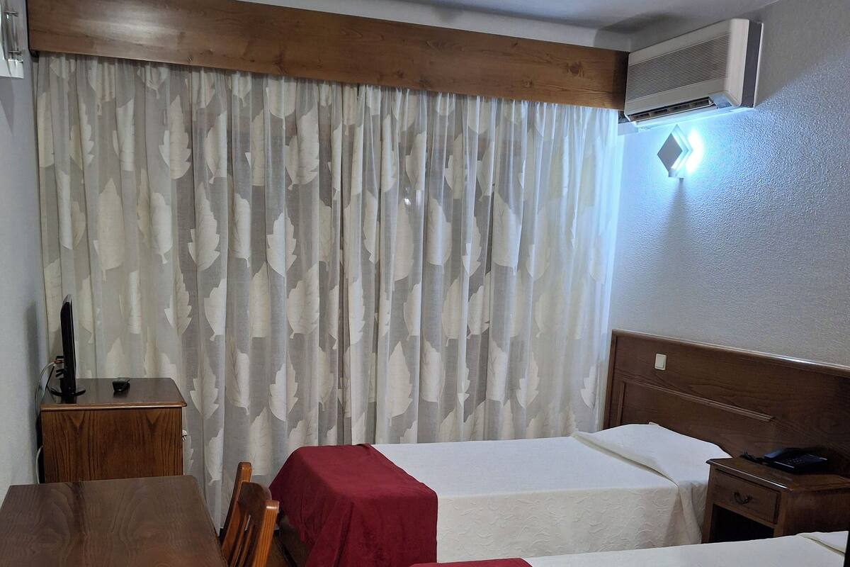 A hotel room with two single beds, a wooden table, and a TV.
