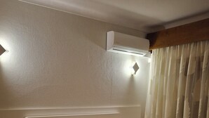 Una habitación de hotel con una cama, mesitas de noche, un teléfono, un aire acondicionado y una cortina.