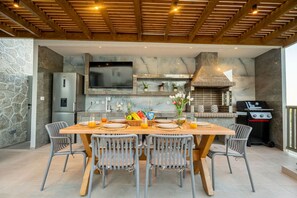 Una cocina exterior moderna con pared de piedra, televisor y parrilla.