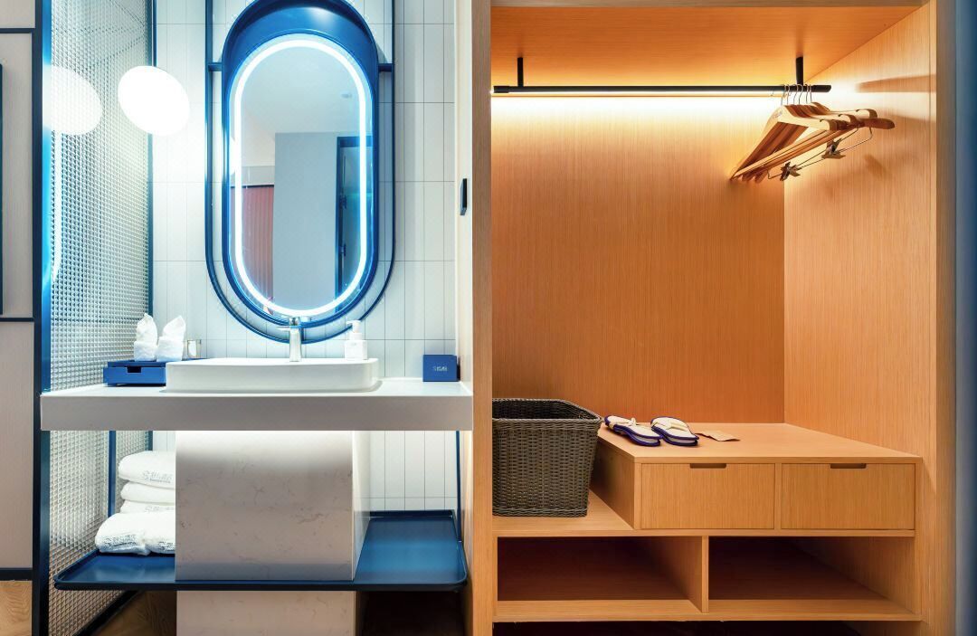 Un baño moderno con un espejo redondo, un lavabo y un mueble de tocador de madera con un perchero para toallas.