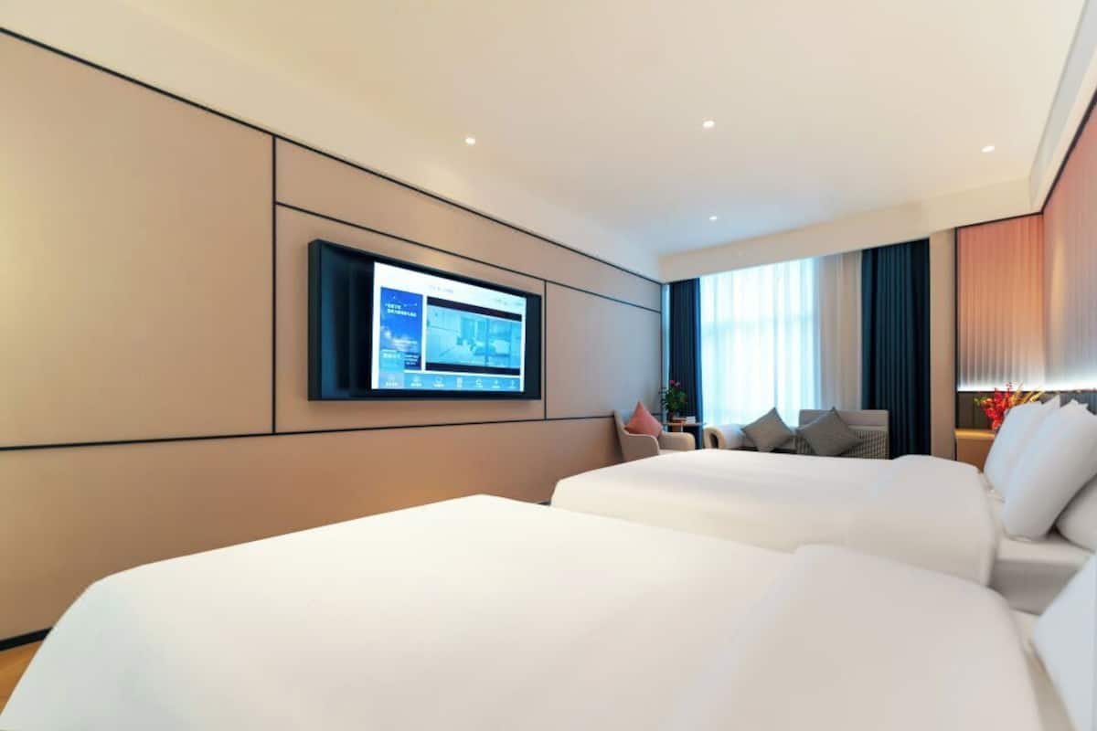 Une chambre d’hôtel avec deux lits, un téléviseur fixé au mur et une grande fenêtre avec des rideaux.