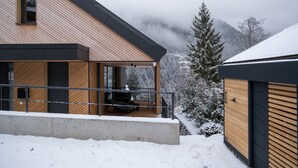 A modern house with a wooden exterior, a balcony, and a snowy landscape in the background.