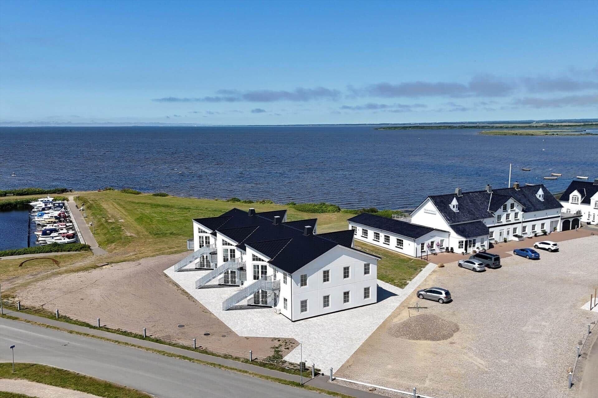Een pand aan de kust met een jachthaven, een groot wit gebouw met veel ramen en een parkeerplaats.