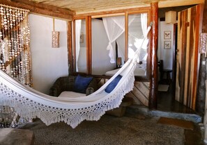 A hammock in a room with a rustic wooden ceiling, a stone floor, and a view through a doorway. - Pousada Shangri-lá (Itacaré)