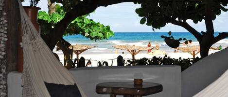 A hammock under a tree, a wooden stool, and a beach view with umbrellas.