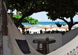 A hammock under a tree, a wooden stool, and a beach view with umbrellas. - Pousada Shangri-lá (Itacaré)