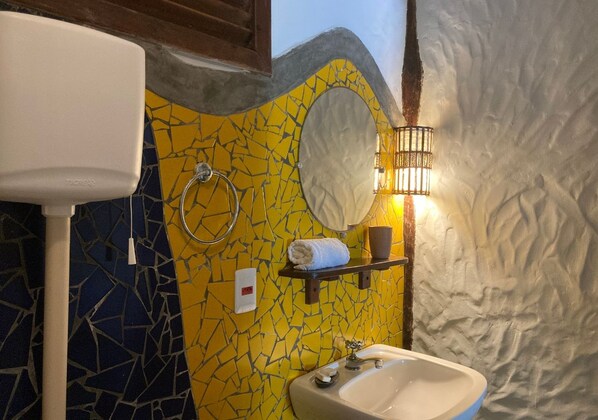 A bathroom with a mosaic wall, a white sink, a mirror, and a towel rack. - Pousada Shangri-lá (Itacaré)