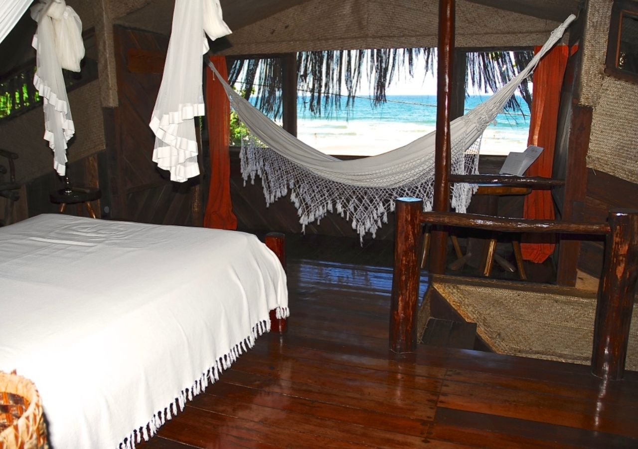 A room with a bed, a hammock, and a view of the beach.