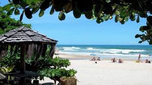 Una playa con una cabaña de techo de paja, arena y olas del océano.