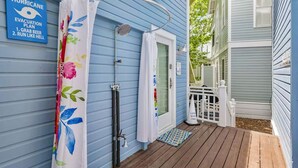 A blue house with a hurricane evacuation plan sign, a shower with a floral curtain, and a wooden deck. - Amazing Porches, Outdoor Dining, & Tower in Seaside, FL! 2 Kings! 2 Bikes! (Santa Rosa Beach)