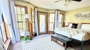 Quarto com cama, banqueta, mesa de cabeceira e ventilador de teto.