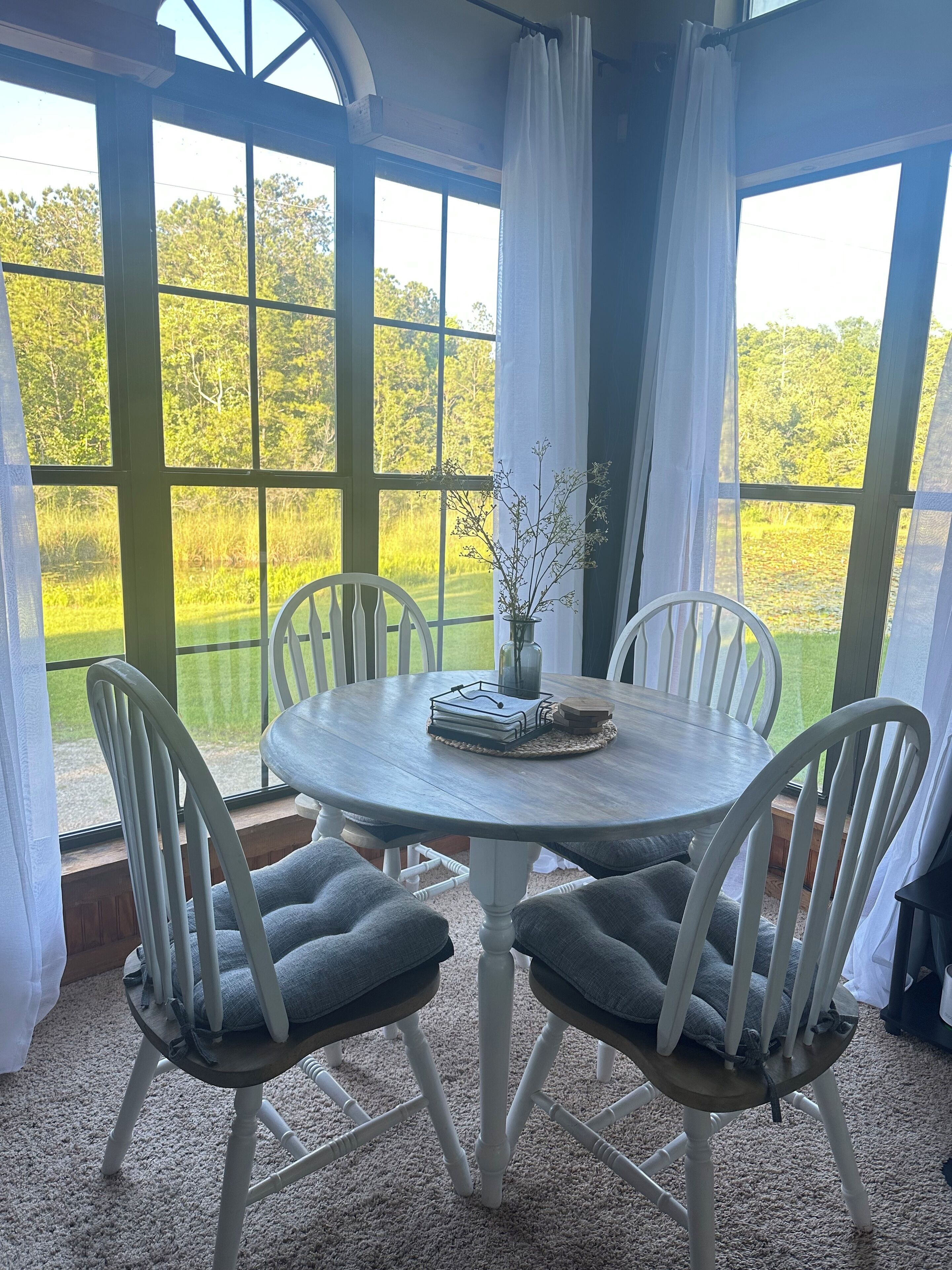 Une table ronde avec quatre chaises, un vase orné de branches et une pile de livres posée sur la table.