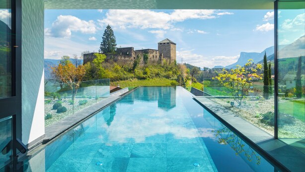 A modern pool with a clear view of a historic castle in the background. - Hotel Der Waldhof in Völlan (Lana)