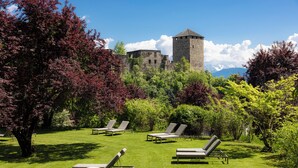 A castle with a tower, surrounded by lush greenery and four lounge chairs on a well-manicured lawn. - Hotel Der Waldhof in Völlan (Lana)