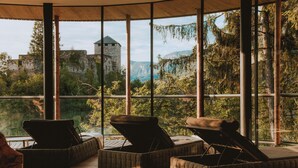 A room with large windows overlooking a castle and forested mountains. - Hotel Der Waldhof in Völlan (Lana)