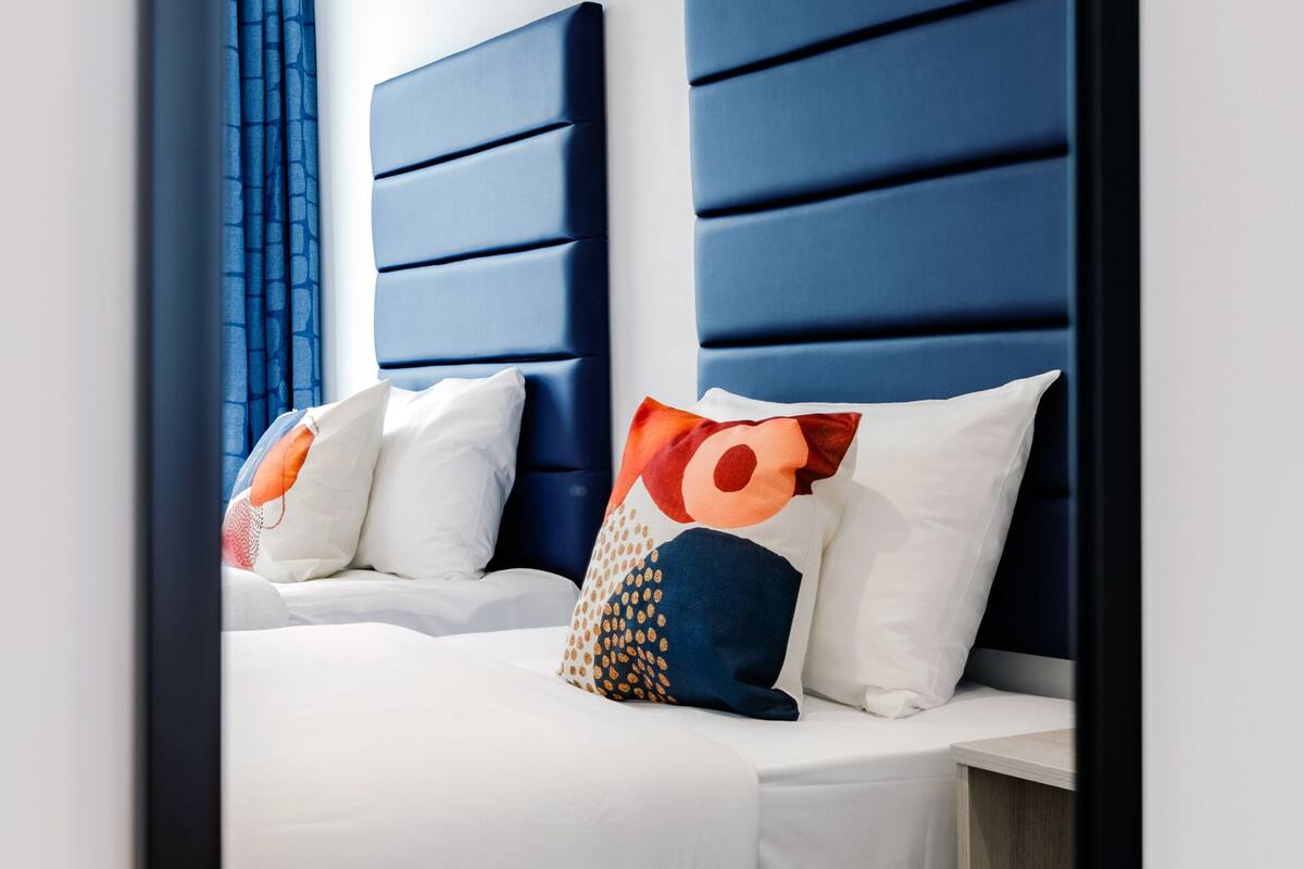 A hotel room with two beds, each with a blue headboard and white bedding.