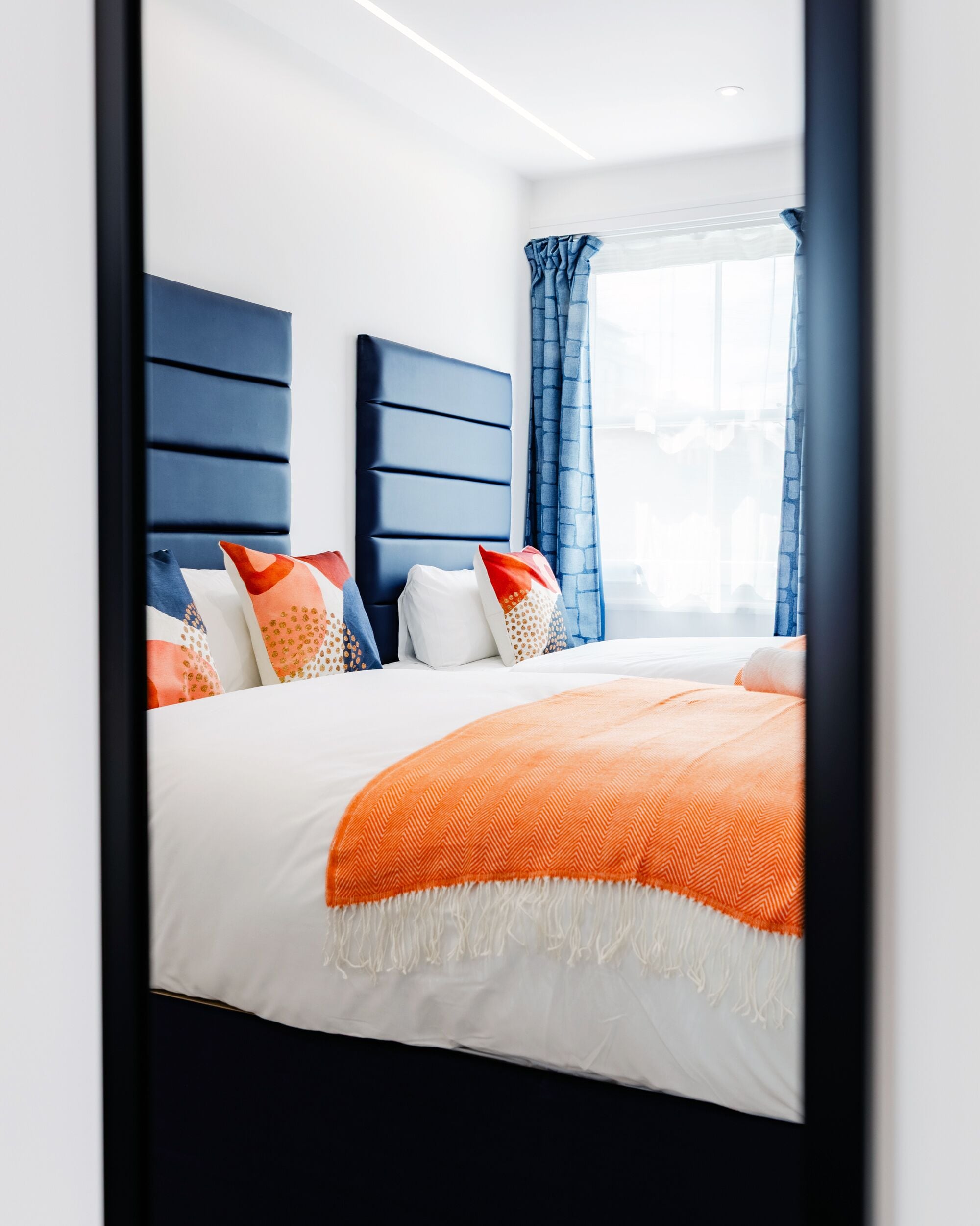 A modern bedroom with a large bed, a headboard, and a window with curtains.