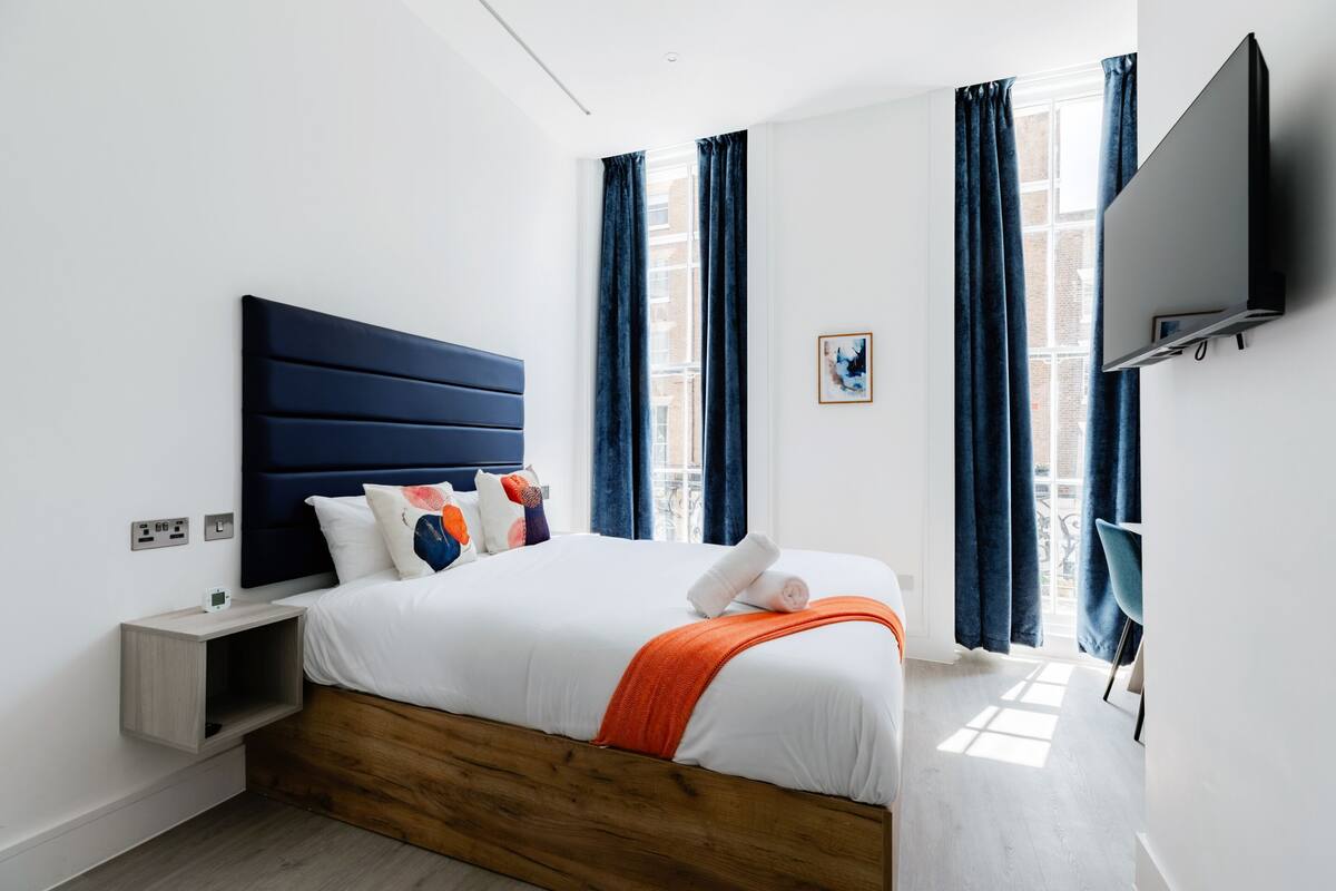 A modern bedroom with a wooden headboard, a white bedspread, and blue curtains.