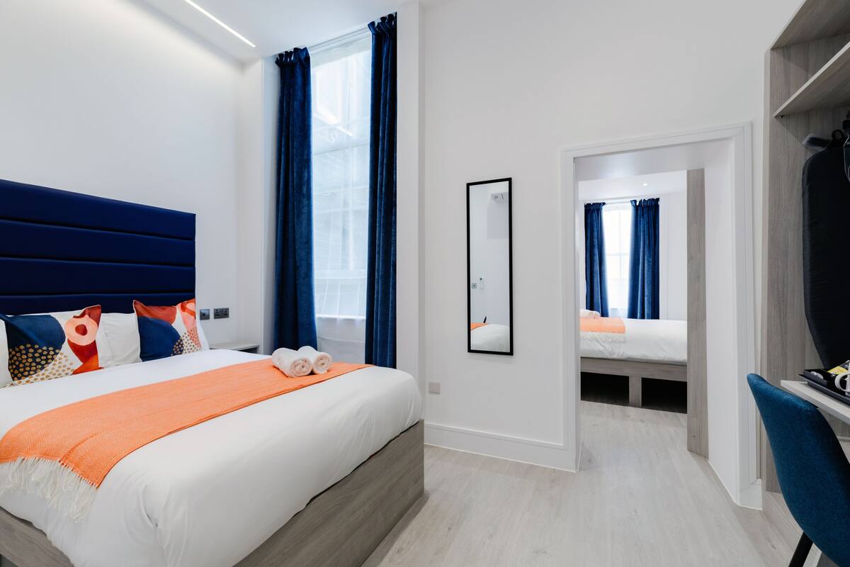 A modern hotel room with a large bed, a desk, and a mirror.