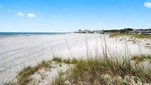 A beach with a clear sky, sandy shore, and buildings in the background. - Cozy Beach living with Breathtaking Ocean and Marsh Views, Sleep 4 (Myrtle Beach)