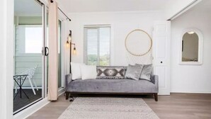 A cozy living room with a grey sofa, patterned cushions, a woven wall hanging, and a large window with blinds. - Cozy Beach living with Breathtaking Ocean and Marsh Views, Sleep 4 (Myrtle Beach)