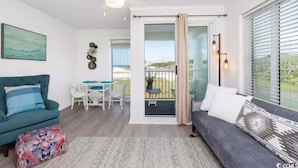 A modern living room with a sofa, a coffee table, and a dining area. - Cozy Beach living with Breathtaking Ocean and Marsh Views, Sleep 4 (Myrtle Beach)