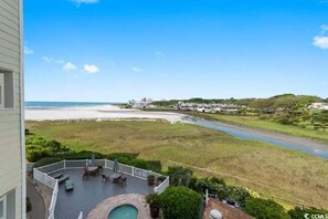 A view from a balcony overlooking a beach, a river, and a residential area with houses and greenery.