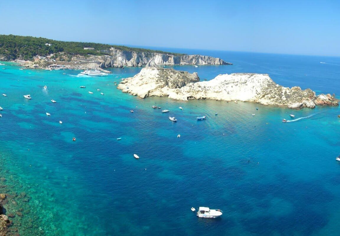 A coastal area with boats, rocky cliffs, and clear blue waters.