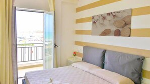 Habitación de hotel con cama, mesita de noche, un cuadro y vistas al exterior.