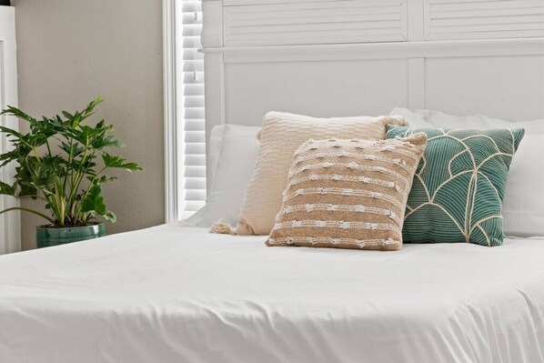 Cozy bedroom showcases a comfortable bed with textured pillows and a leafy green plant, creating a serene atmosphere.
