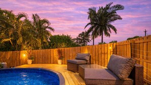 Un jardin avec une piscine, une terrasse en bois, des meubles en osier et une clôture en bois.