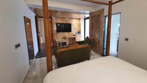 A bedroom with a four-poster bed, a television, a wooden cabinet, and a green sofa. - Hotel Daffodils Inn (Dehradun)