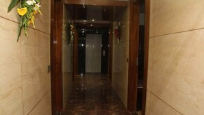 A hallway with marble flooring and wooden walls, leading to an elevator. - Hotel Daffodils Inn (Dehradun)