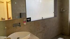 A modern bathroom with a large mirror, a sink, and a shower area. - Hotel Daffodils Inn (Dehradun)