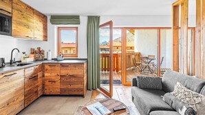 A modern kitchen with wooden cabinets, a built-in microwave, and a large window. - Atelier Wilder Kaiser | Pool, sauna & mountain view (Reit im Winkl)