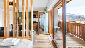 A modern bedroom with a wooden floor, a large sliding glass door leading to a balcony, and a view of the outdoors. - Atelier Wilder Kaiser | Pool, sauna & mountain view (Reit im Winkl)