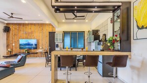 Une cuisine moderne avec un mur d’accent en bois, un coin repas avec des tabourets de bar et un téléviseur fixé au mur.